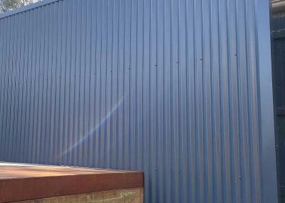 Tall grey corrugated metal fence beside the timber-clad edge of a deck