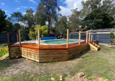 Hardwood deck being built around an above-ground pool with timber-clad sides