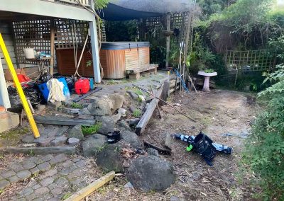 Overgrown backyard with old sleepers, rocks and tools beside a spa