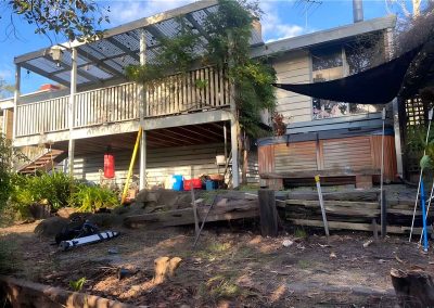 Sloping backyard with old sleeper walls below a raised veranda and spa