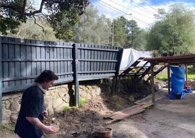 Man beside a dark timber fence on a stone retaining wall during works