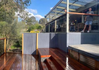 Oiled hardwood deck with steps, a spa and grey screens below a veranda