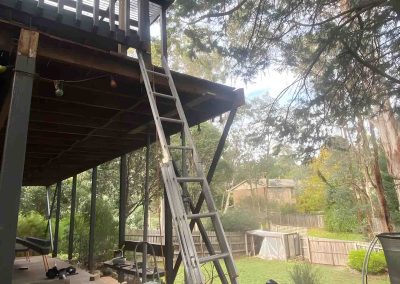 Worker beside a ladder under an elevated timber balcony