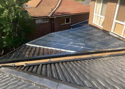 New dark metal pergola roof between the tiled roofs of a brick house