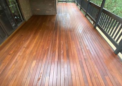 Long oiled hardwood balcony deck with a dark balustrade beside glass doors