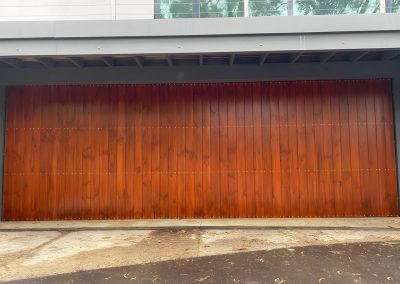 Garage door clad in stained timber boards under a balcony