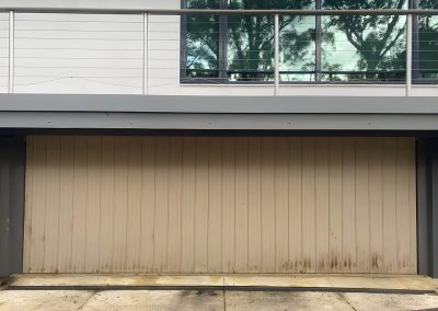 Old beige garage door under a house with a balcony above