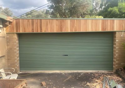 Green roller door on a double garage with new timber cladding above