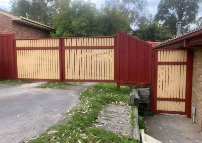 Red and cream timber fence and gates across a driveway
