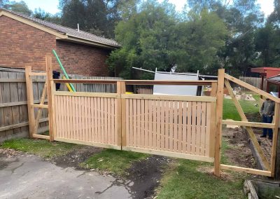 New timber picket fence and gate frame going up beside a brick house