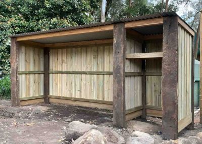 Open-fronted woodshed with sleeper posts, paling walls and a metal roof