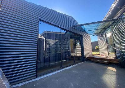 Finished extension clad in dark corrugated metal with large glass doors