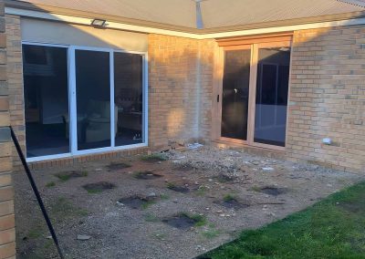 Bare backyard corner of a brick house with pier holes dug for a deck