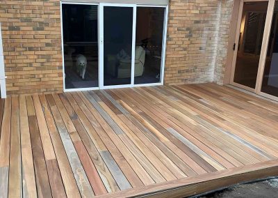 New unoiled hardwood deck in the corner of a brick house