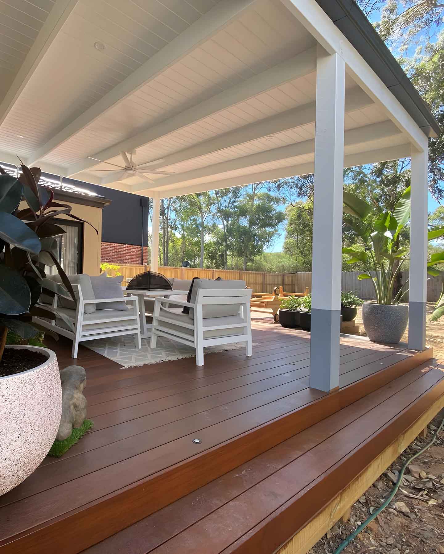 Covered timber deck with white posts, outdoor chairs and pot plants