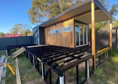 Black steel deck frame in front of a timber-clad backyard studio