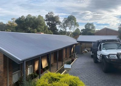 Brick house with a long grey metal veranda roof beside a paved driveway