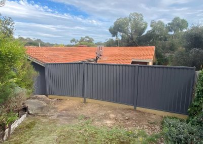 Grey metal panel fence along the back of a sloping garden