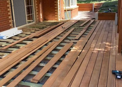 Hardwood deck boards being laid on the subframe beside a brick house