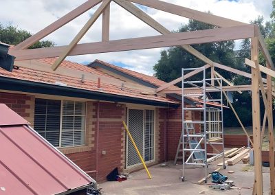 Gable pergola frame going up beside a brick house with scaffolding