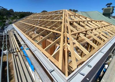 New timber roof trusses on an extension beside a green metal roof