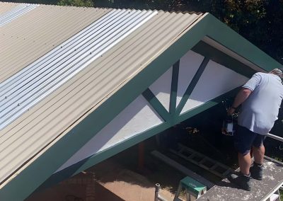 Worker fitting roofing to a gable pergola with green trim