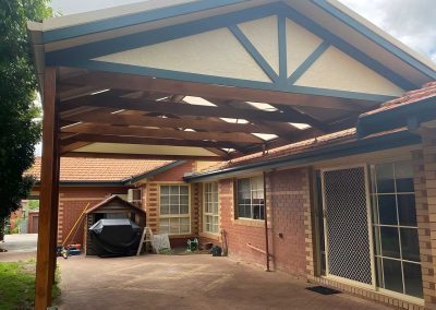 Finished gable pergola with a green-trimmed gable over a paved area