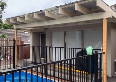 Pergola with timber rafters beside a pool with a black pool fence
