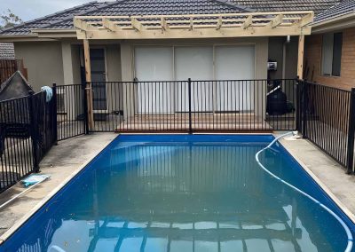 In-ground pool with a black pool fence and a pergola behind