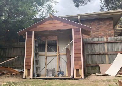 Gabled garden shed frame being built against a paling fence