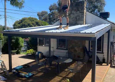 Worker standing on a new metal pergola roof over a timber deck