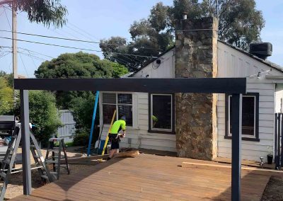 Steel-framed pergola going up over a timber deck beside a weatherboard house