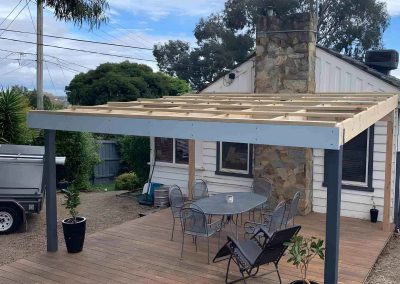 Pergola frame with timber rafters over a deck with outdoor furniture