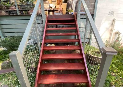 Red timber stairs with grey handrails leading up to a covered deck