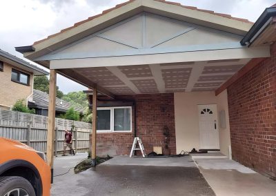 Gable carport with a lined ceiling over a driveway beside a brick house