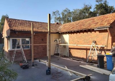 Timber posts and beams going up beside a brick house, with ladders
