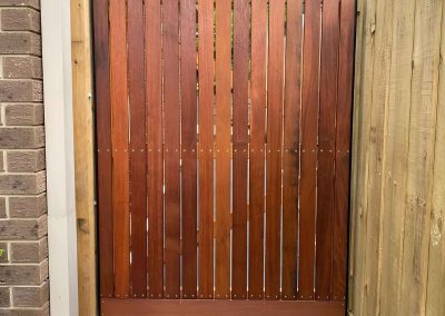 Stained hardwood side gate between a brick wall and a paling fence