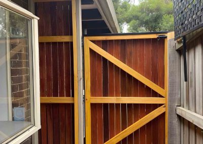 Stained timber side gate with a Z-brace frame beside a matching screen