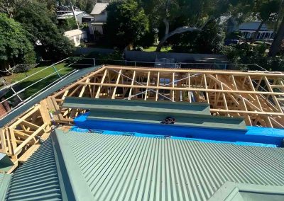 Timber roof trusses going up beside new green corrugated roofing