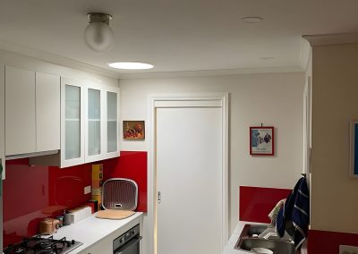 Galley kitchen with white cupboards and a red splashback