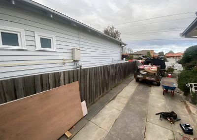 Side driveway of a weatherboard house with an old paling fence and materials
