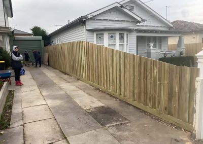 New treated pine paling fence along a weatherboard house driveway