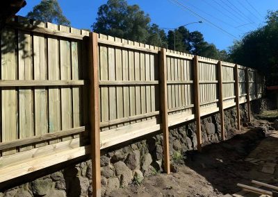 New treated pine paling fence along a stone retaining wall