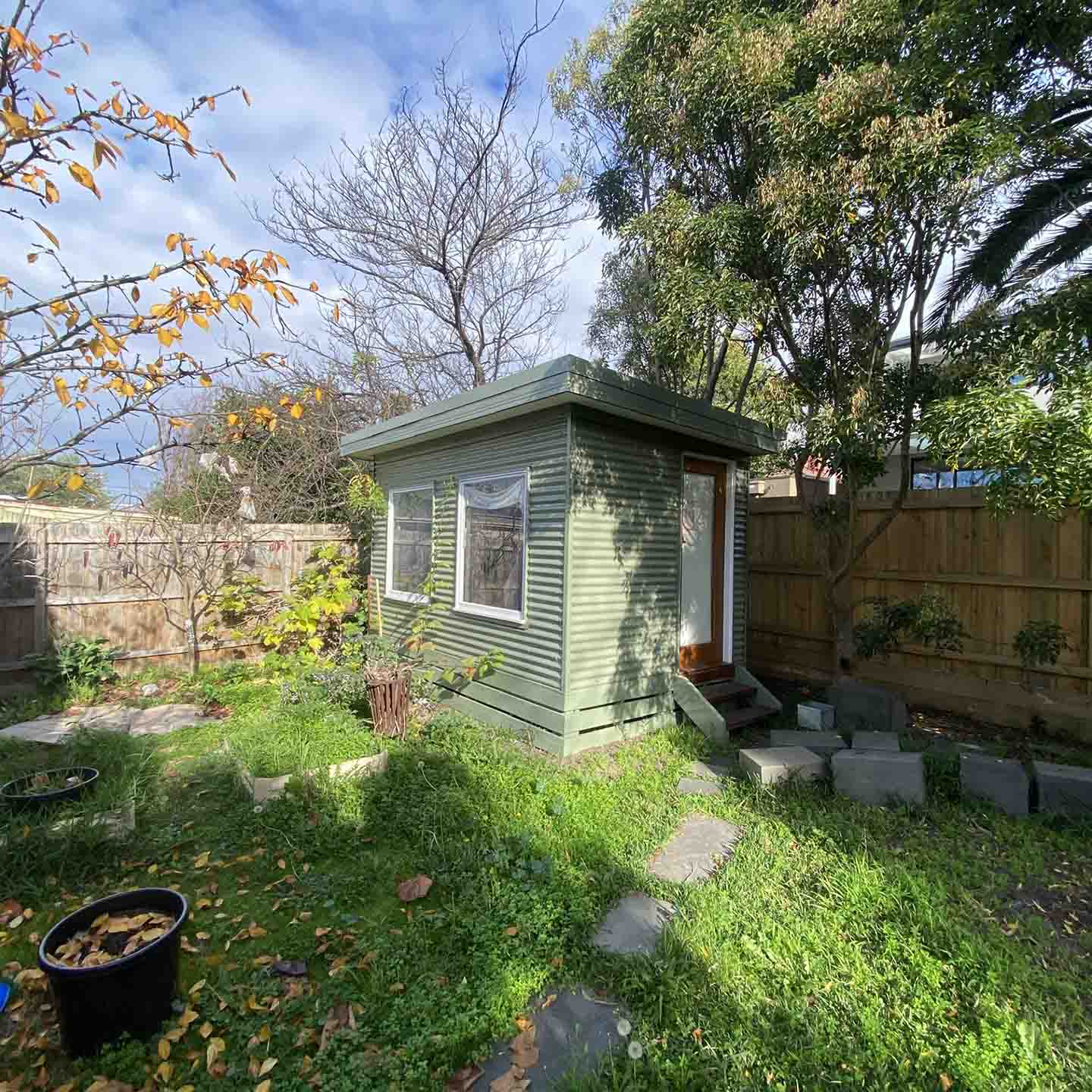 After: green weatherboard backyard studio with a window and small steps