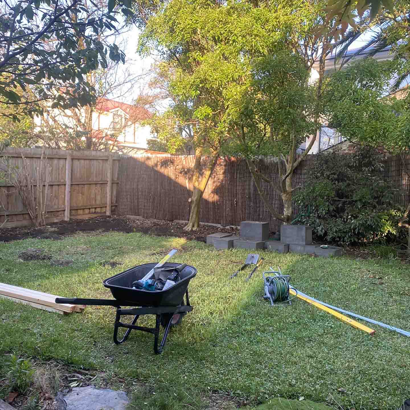 Before: grassy backyard with a wheelbarrow, tools and concrete blocks