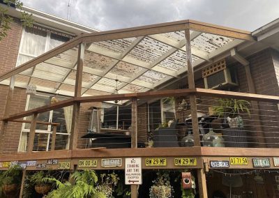 Before: old pergola with worn roof sheets over a raised deck, wider view