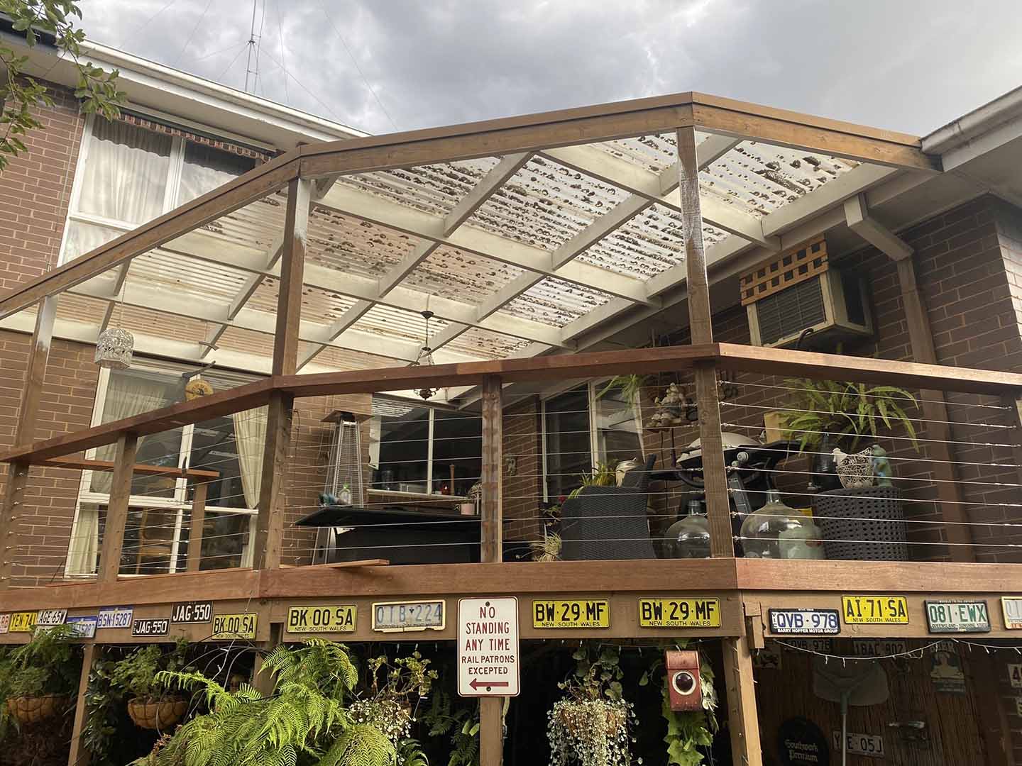 Before: old pergola with worn roof sheets over a raised deck, wider view